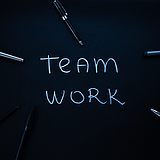 "Team work" steht auf einem Tisch geschrieben, auf dem Schreibmaterial herumliegt